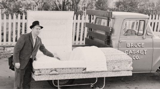 Vintage photo of Bruce Elder beside a casket in front of a Bruce Casket Co. truck.
