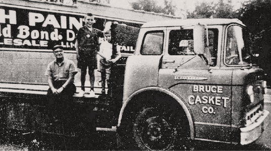 Vintage photo of Bruce Elder with two children on back of Bruce Casket Company truck.