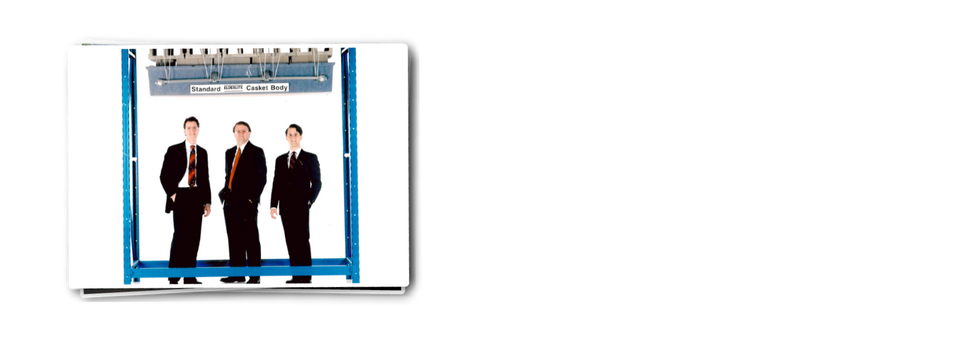 Vintage photo of the founders of Elderlite Casket dressed in black suits, Mark Elder, Gerald Edler and Alan Elder standing under an Elderlite casket with several cinder blocks on top.