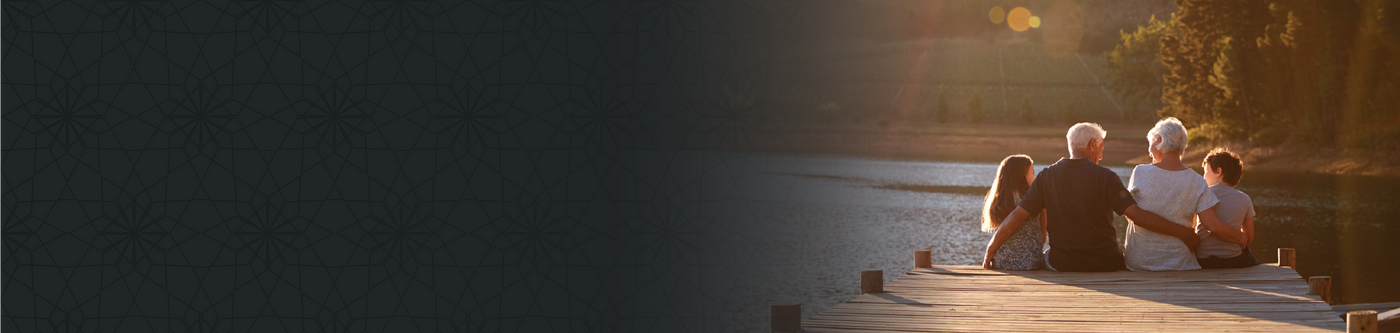 Four people sitting on a lakeside dock at sunset, looking out over the water.